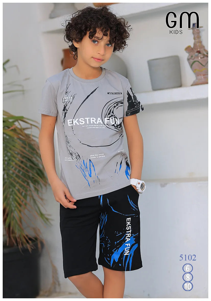 Child wearing a gray t-shirt and black shorts with blue designs, standing indoors.
