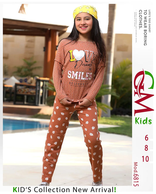 Young girl wearing a brown polka dot shirt with text and a yellow headband, standing outdoors.