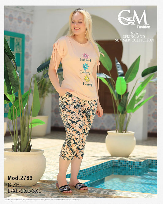 Woman in floral capri pants and light top standing by a pool with plants around.