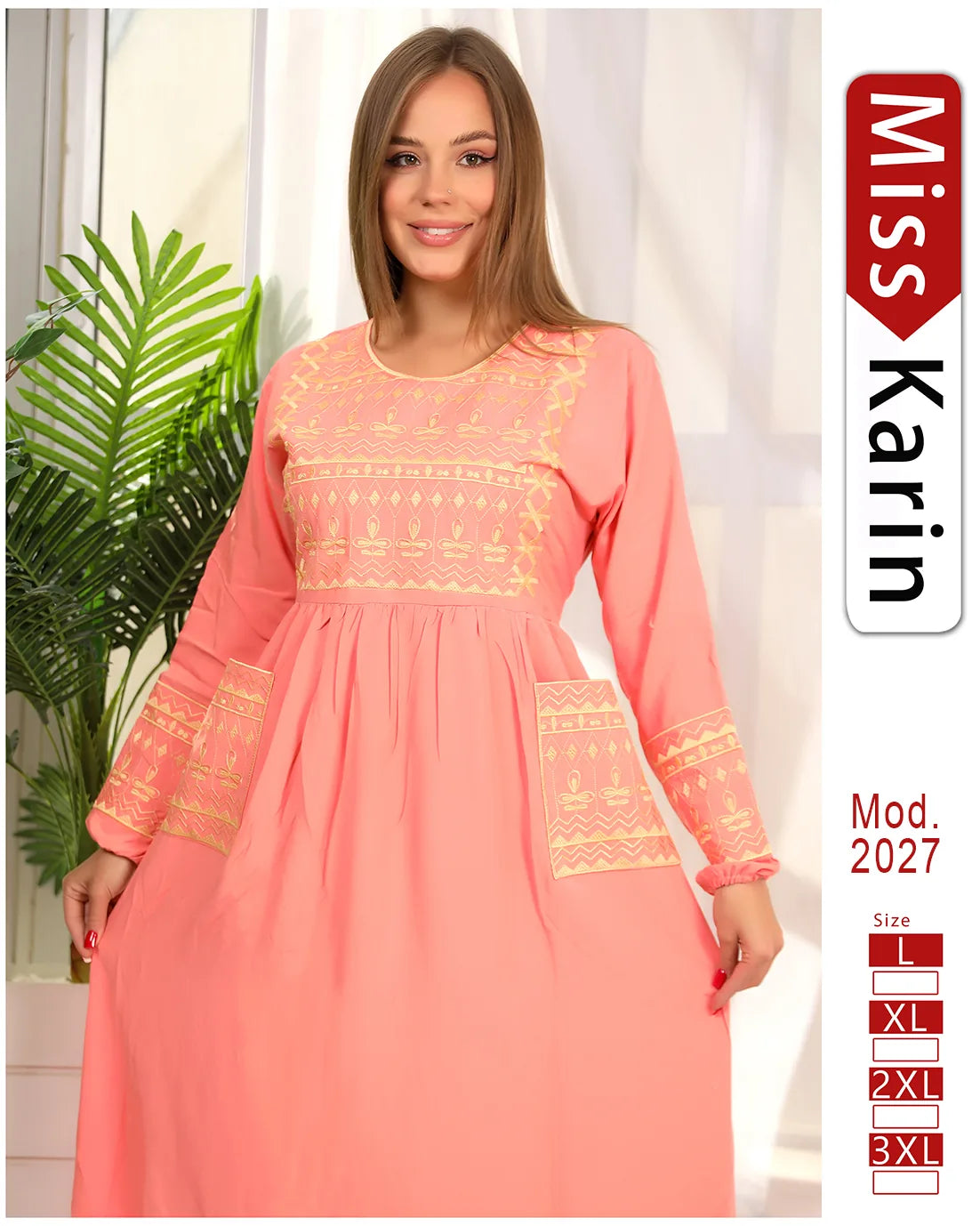 Woman wearing a pink dress with yellow embroidery, standing indoors with a plant in the background.