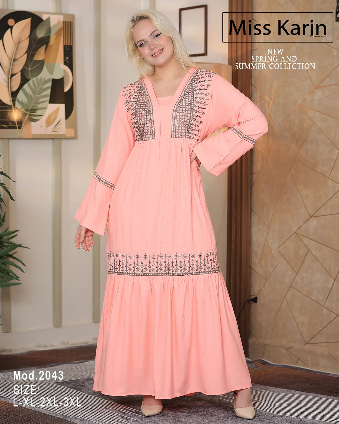 Woman wearing a pink dress with embroidery, standing indoors with decorative elements in the background.