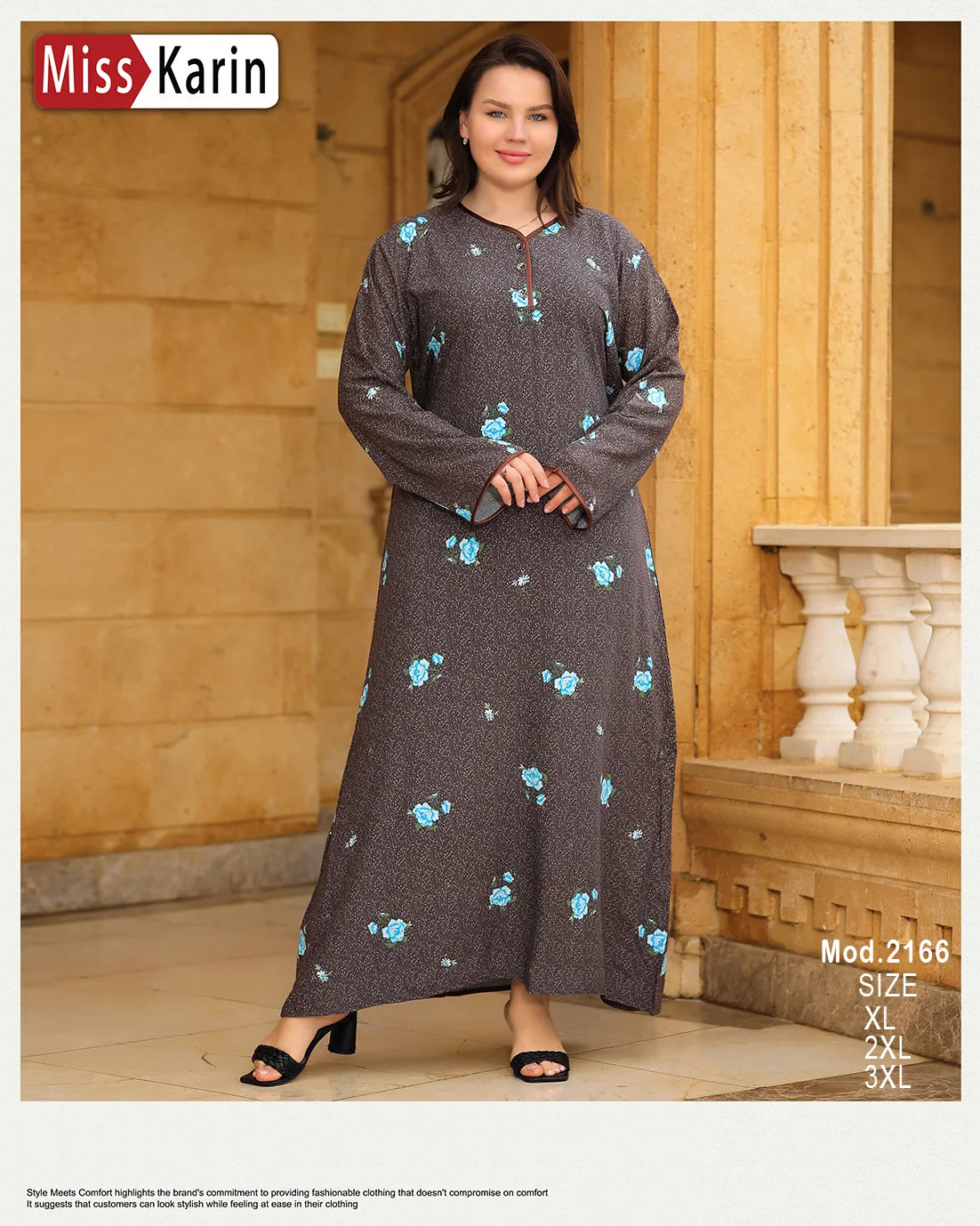 Woman wearing a long dark gray dress with floral patterns in front of a stone wall.