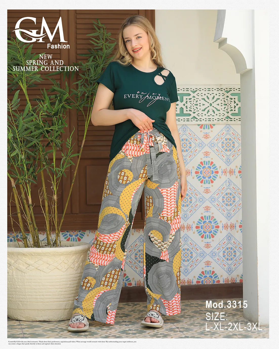 Woman wearing a green top and patterned pants standing in front of a decorative wall with plants.