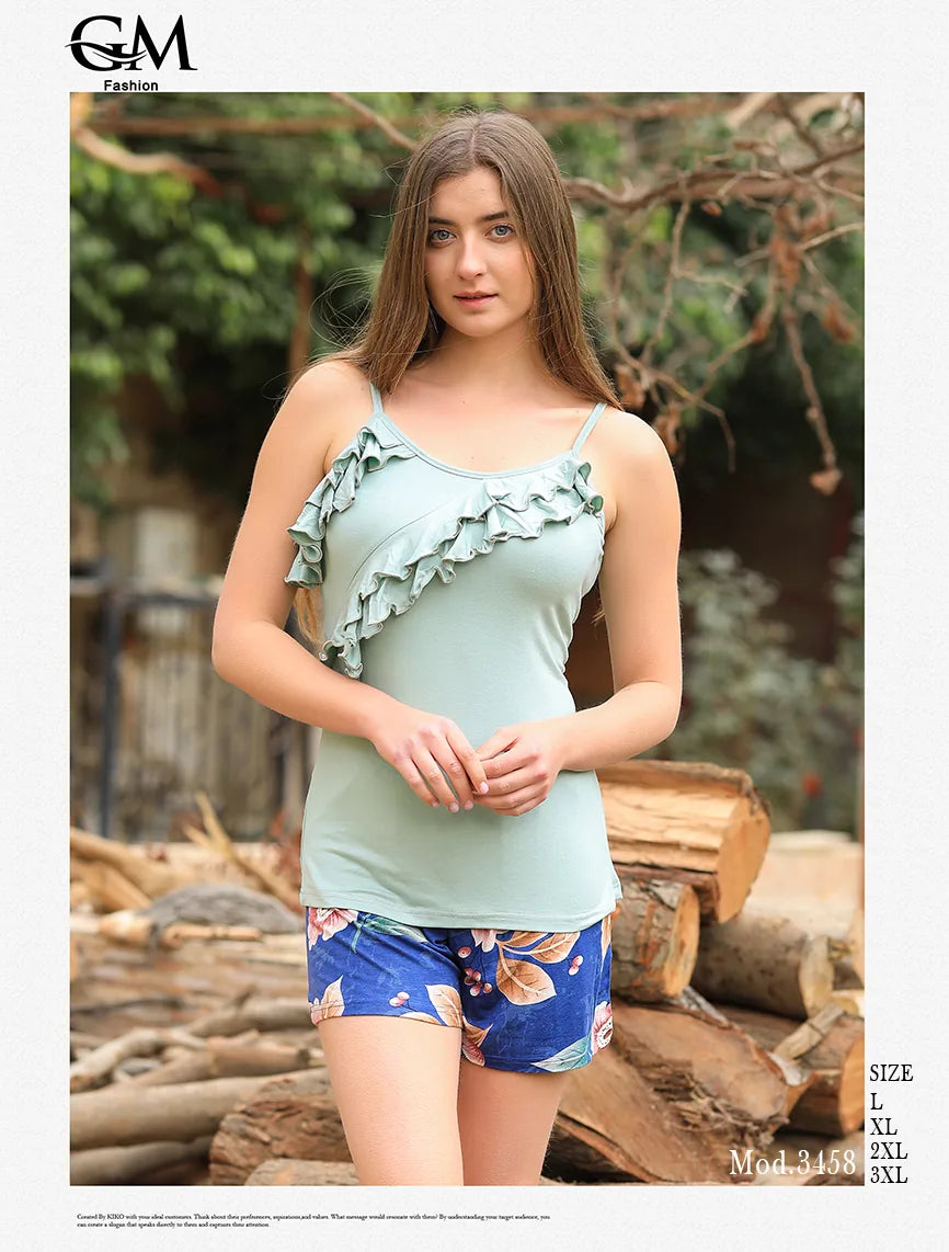 Woman wearing a light blue top with ruffles and floral shorts, standing outdoors with logs in the background.