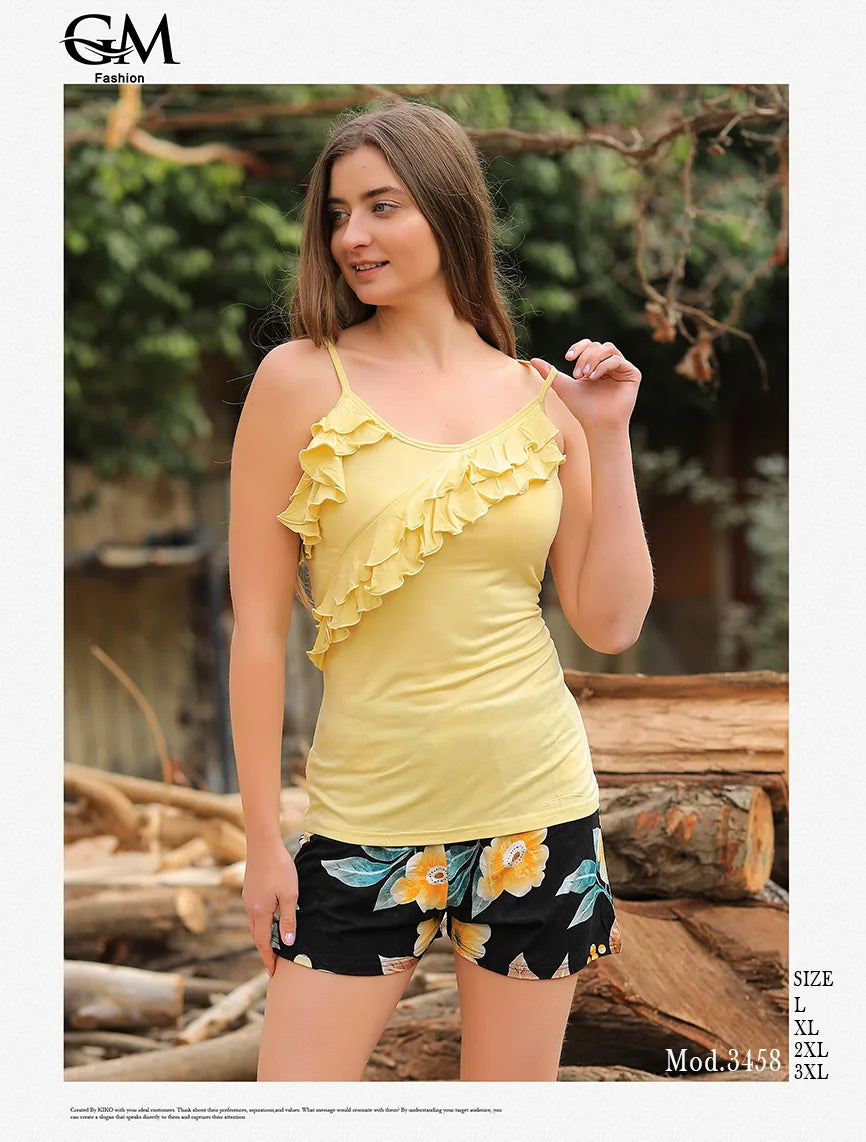Woman wearing a yellow ruffled top and floral shorts outdoors with logs and greenery in the background.