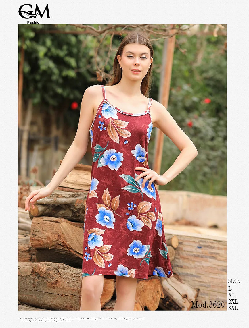 Woman wearing a floral dress standing outdoors with wooden logs and greenery in the background