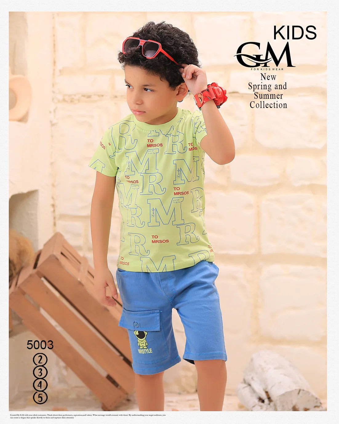 Child wearing a green shirt with text and blue shorts, standing indoors with a neutral background.