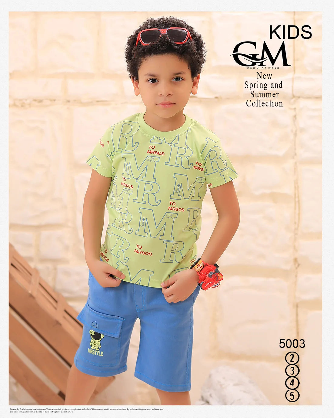 Child wearing a green shirt with red text and blue shorts, standing against a light-colored wall.