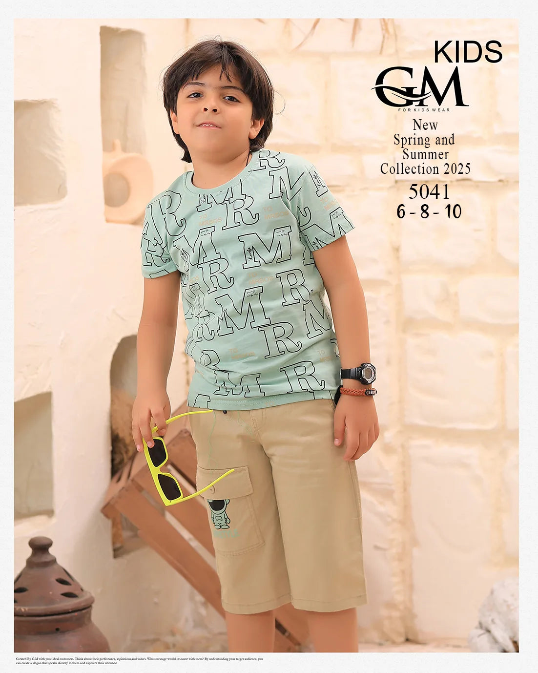 Child wearing a light blue t-shirt with letter pattern and beige shorts, holding sunglasses, against a neutral background.