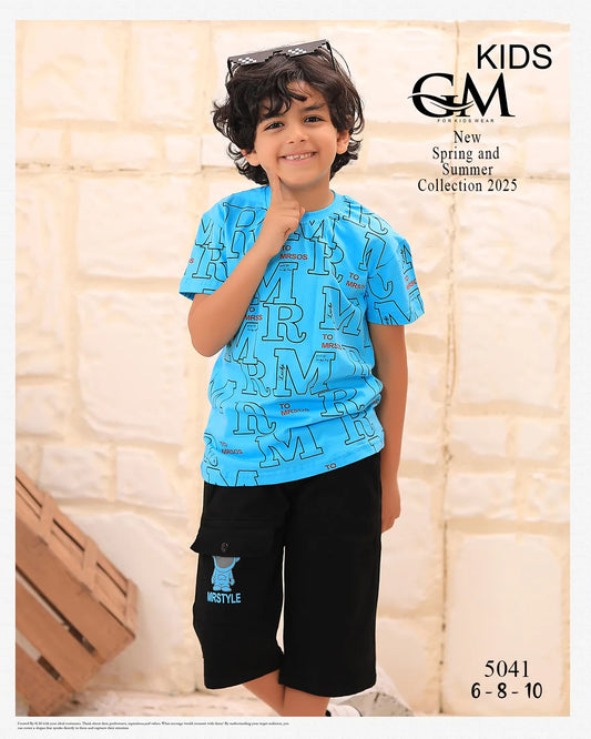 Child wearing a blue shirt with text and black shorts, standing against a stone wall with 'GM' branding.