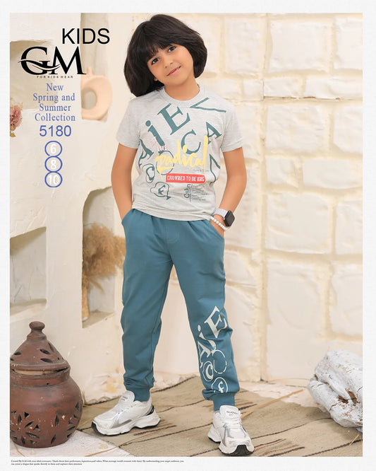 Child wearing a gray t-shirt and blue pants with 'G&F' branding, standing against a stone wall.