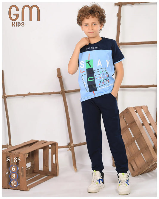 Child wearing a blue and black t-shirt with text and graphics, standing in front of wooden crates.