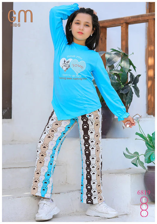 Child wearing a blue long-sleeve top and patterned pants standing outdoors.