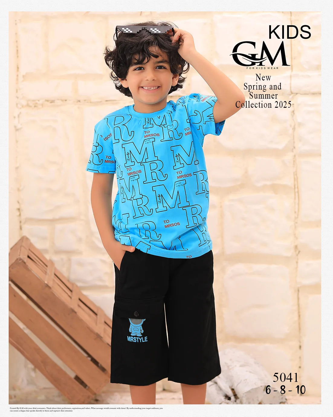 Child wearing a blue shirt with text and black shorts, standing against a stone wall with 'GM' branding.