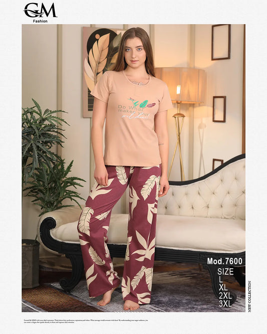 A woman wearing a peach t-shirt with text and teal pants with a leaf pattern in a room setting.