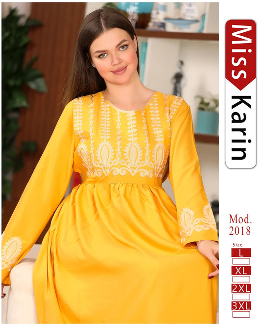 Woman wearing a yellow dress with white embroidery, sitting indoors.