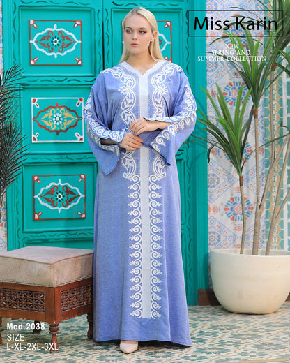 Woman wearing a blue embroidered dress with a decorative green wall in the background, featuring 'Miss Karin' branding.