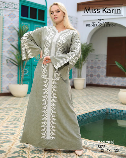 Woman wearing a long, light-colored embroidered dress in a decorative setting with plants and a pool.