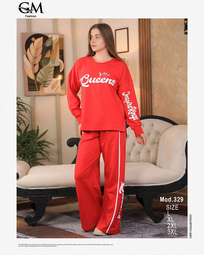 Woman wearing a red 'Queens' tracksuit in a living room setting with GM Fashion branding.
