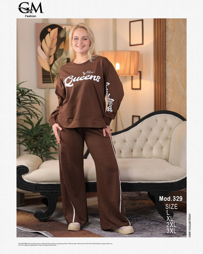 Woman wearing a brown outfit with 'Queens' text in a living room setting, featuring GM Fashion branding.