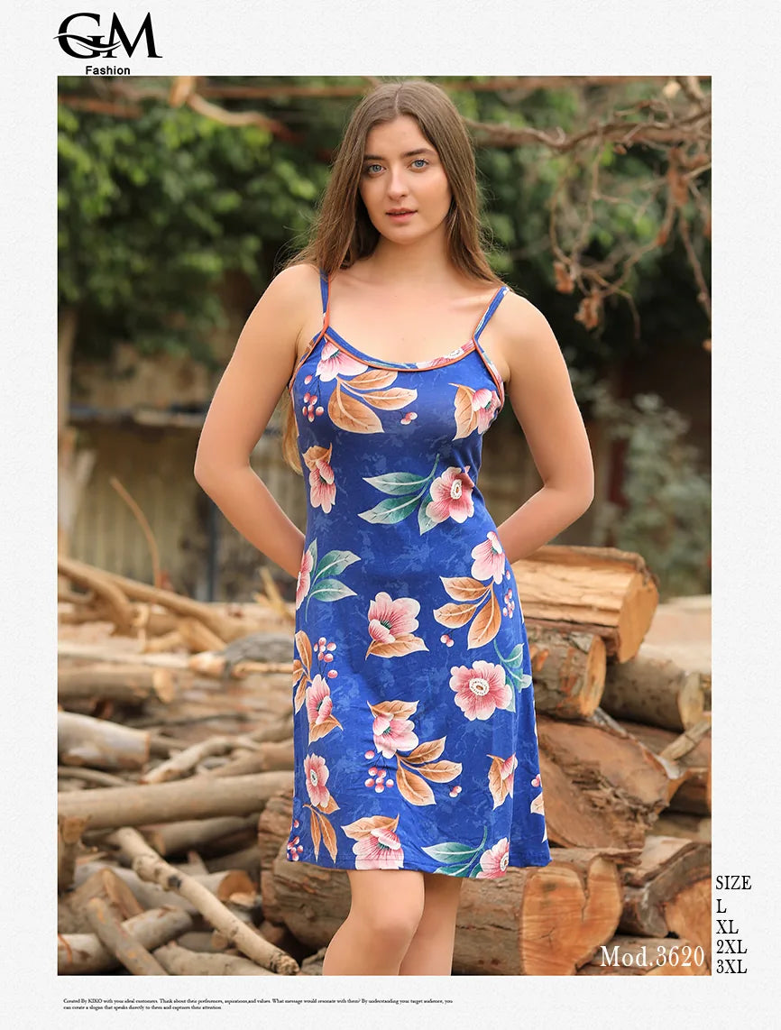 Woman wearing a blue floral dress standing outdoors with logs and greenery in the background