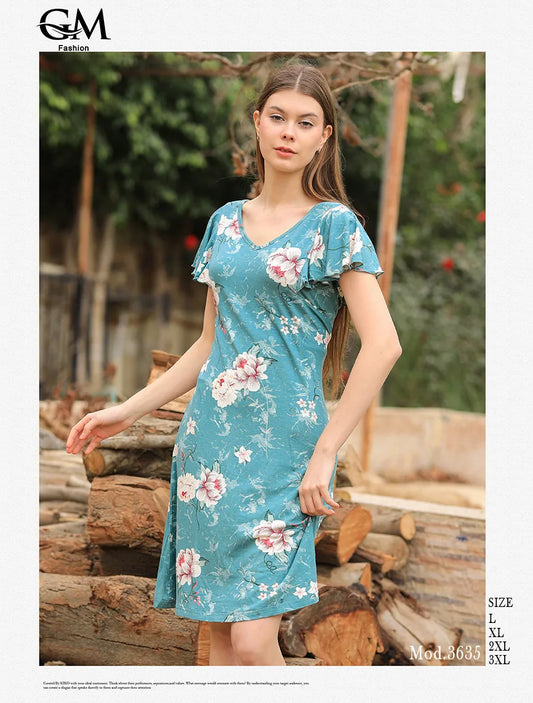 Woman wearing a floral dress standing outdoors with logs and greenery in the background