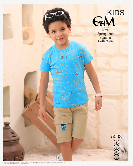 Child wearing a blue shirt and beige shorts with sunglasses on head, standing indoors.