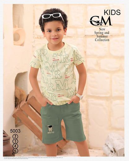 Child wearing a patterned shirt and green shorts with sunglasses on head, standing indoors.