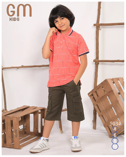 Child wearing a red checkered shirt and green shorts standing in front of wooden crates.