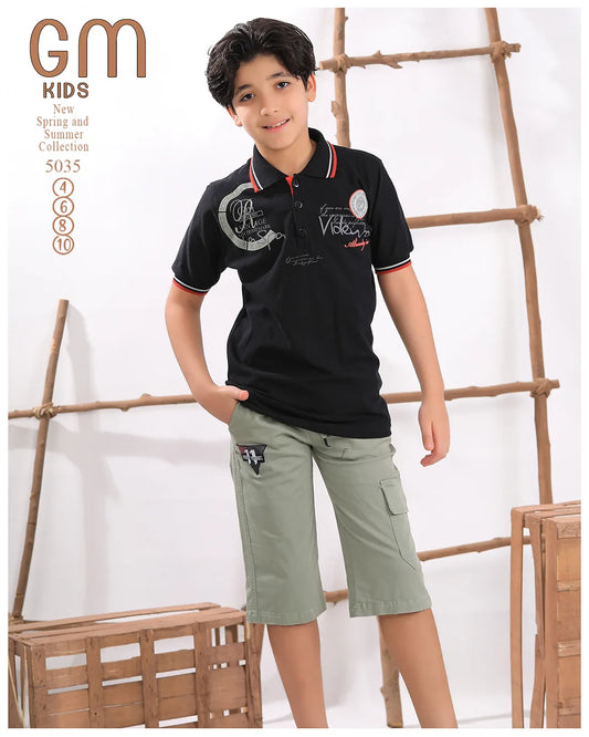Child wearing a black polo shirt and green shorts with a wooden ladder and basket in the background.