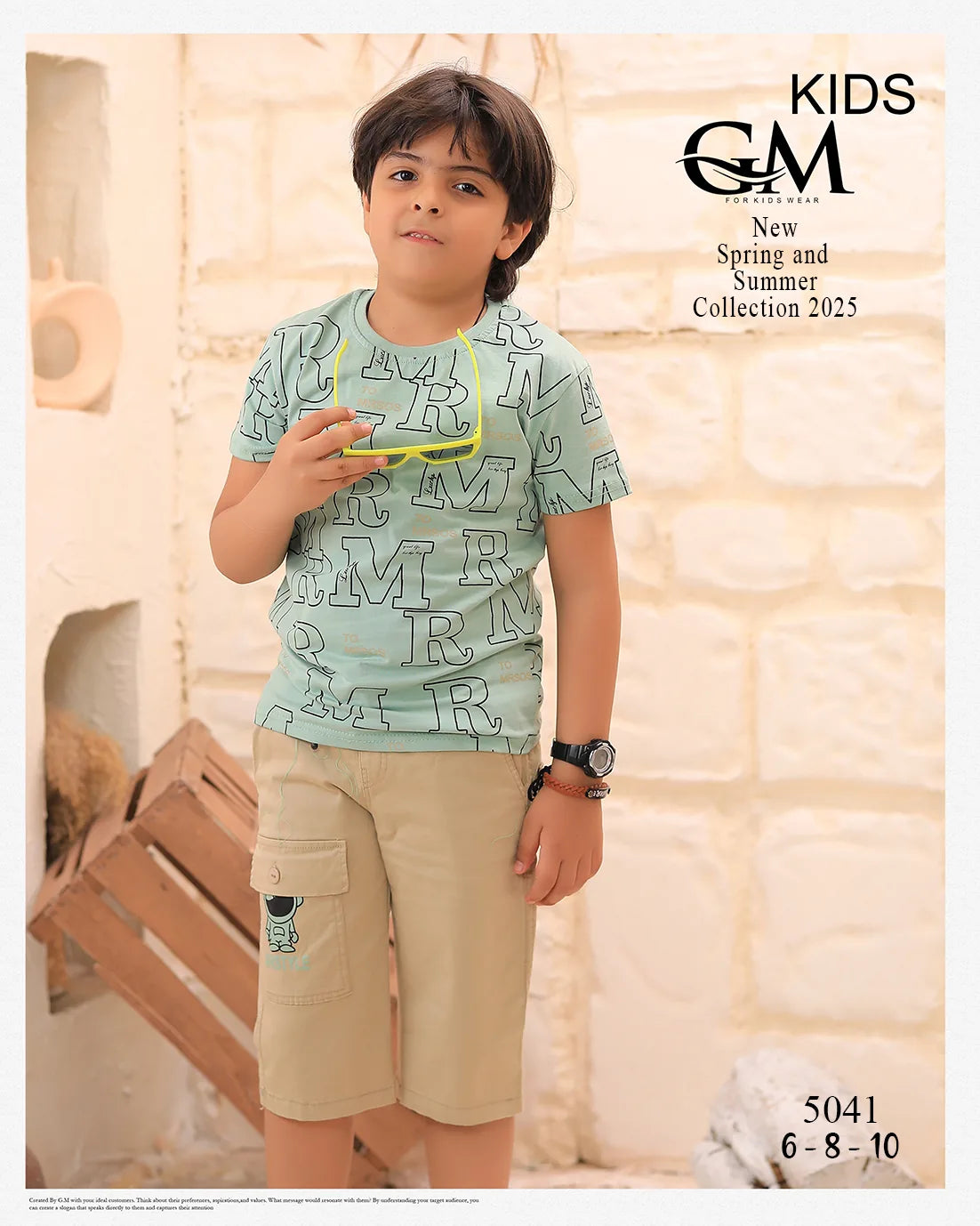 Young boy wearing a light blue t-shirt with letter pattern and beige shorts, standing indoors.
