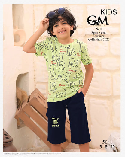 Child wearing a light green t-shirt with text and dark blue shorts, standing indoors.