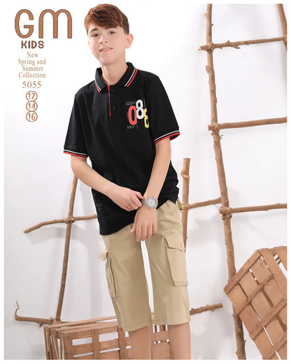 Young boy wearing a black polo shirt with colorful design and beige cargo shorts, standing against a white background with wooden elements.