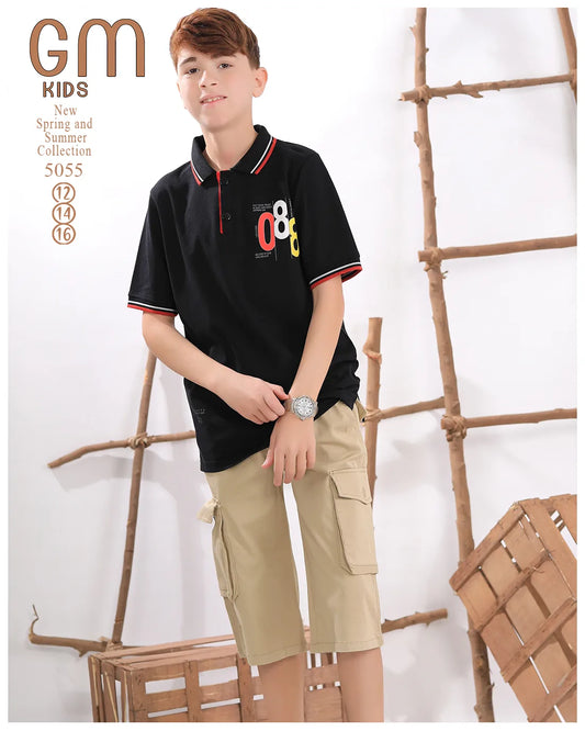 Young boy wearing a black polo shirt with colorful design and beige cargo shorts, standing against a white background with wooden elements.