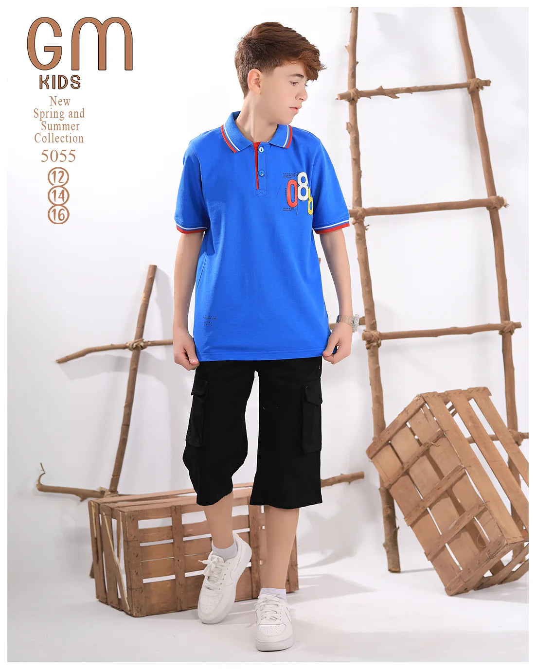 Child wearing a blue polo shirt with colorful design and black shorts, standing against a white background with wooden crates.