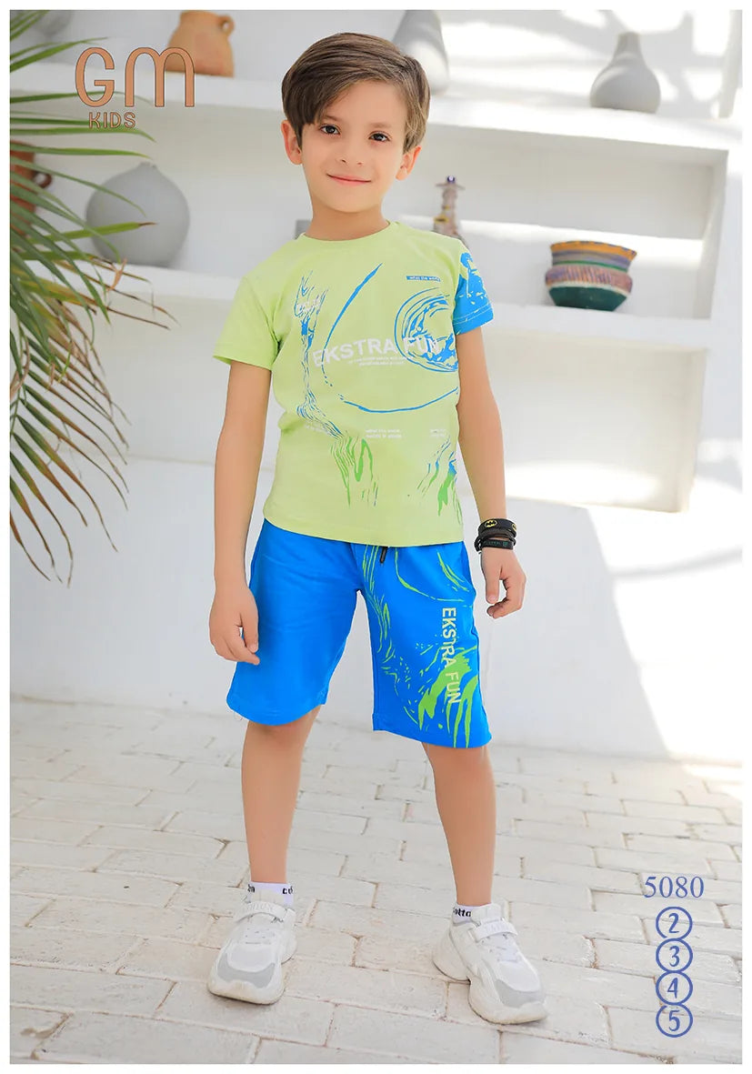 Child wearing a green t-shirt and blue shorts with a graphic design, standing indoors.