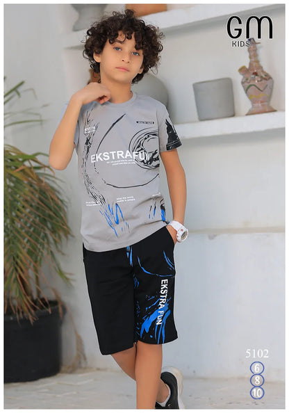 Child wearing a gray t-shirt and black shorts with blue designs, standing indoors.