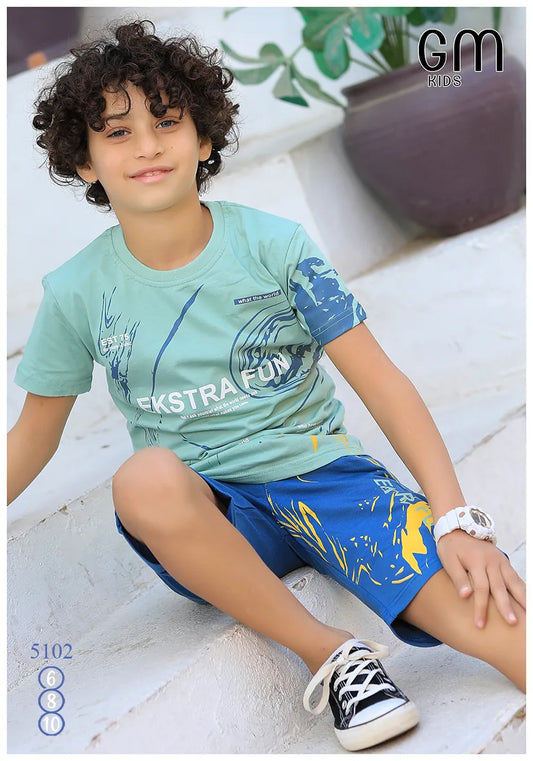 Child wearing a green t-shirt and blue shorts sitting on a stone surface with 'GM Kids' branding.