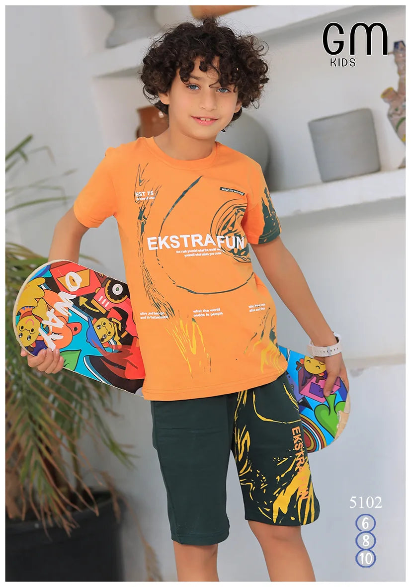 Child wearing an orange shirt and dark shorts with colorful graphics, holding a skateboard, against a white wall.