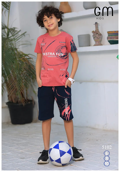 Child wearing a pink 'Ekstra Fun' t-shirt and dark shorts with a plant and shelf in the background.