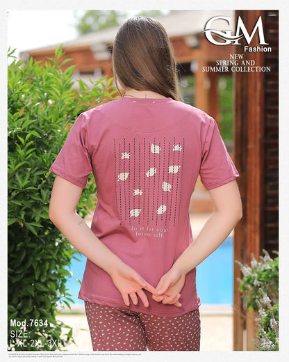 Person wearing a pink t-shirt with a pattern on the back, standing outdoors.