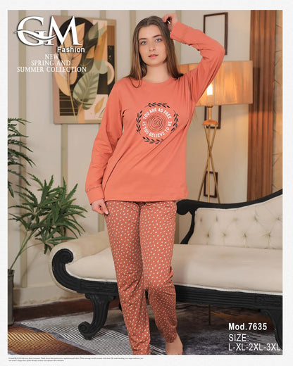 Woman wearing a coral long-sleeve top and patterned pants in a living room setting.